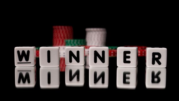 Winner spelled in game dice letters reflected on black background with stacks of poker chips in the background