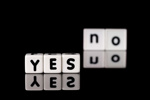 Yes spelled in dice letters in foreground with the word no out of focus in background. Isolated on black background.