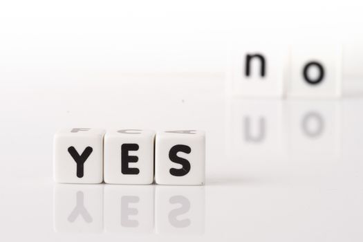 Yes spelled in dice letters in foreground with the word no out of focus in background. Isolated on white background.