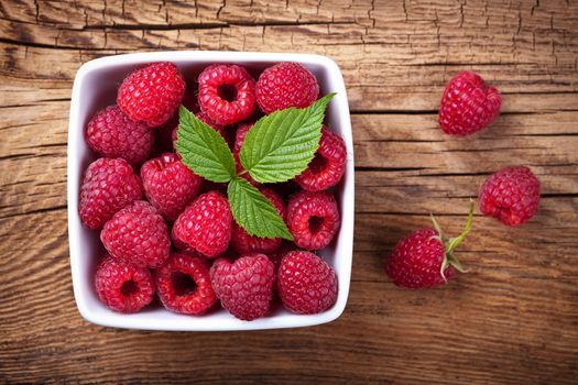 Raspberries in bowl on wooden table background. Top view