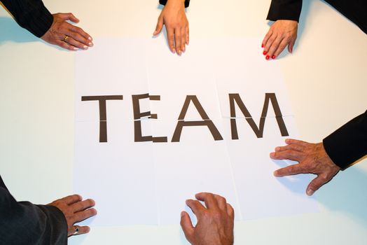 TEAMwork : Hands holding pieces of a puzzle building the word TEAM made out of single papers with the word team spread on them