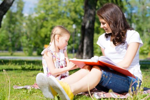 girl with the teacher reading a book together in the summer park