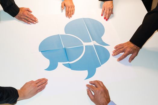 Communication: Hands holding pieces of a puzzle consisting of single papers with speech bubbles spread on them - concept for communication in teams, dialogue and understanding each other