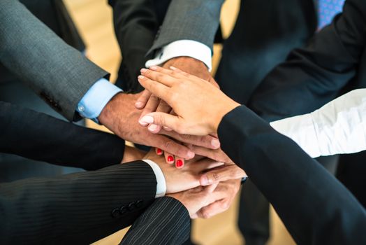 Multiracial group of nine diverse businesspeople standing in a circle facing each other joining hands in a team