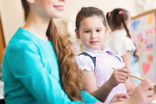 girl interested in drawing the teacher in the background paint other children