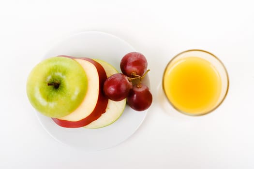 Apple, grapes on a plate and a glass of orange juice. top view