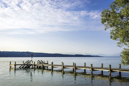 Jetty at lake Starnberg Germany in the morning with forest and mountains in background