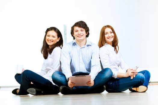 Image of three students in casual wear sitting on floor and smiling