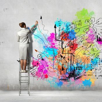 Back view of businesswoman drawing colorful business ideas on wall