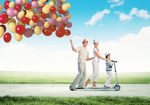 Image of happy young family riding on scooter pulling bunch of colorful balloons