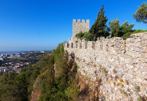 Perimeter fortified stone wall with a lookout tower and crenellations of a castle or fortified walled medieval town with a view out over the valley below