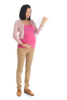 Full body six months pregnant Asian woman using digital computer tablet pc standing isolated on white background.