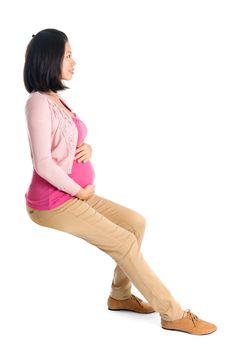 Full body six months pregnant Asian woman sitting on transparent chair, side or profile view,  isolated on white background.