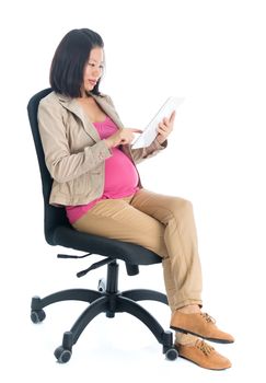 Full body six months pregnant Asian business woman using digital computer tablet pc, sitting on chair isolated on white background.