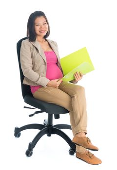 Full body six months pregnant Asian businesswoman holding file folder document seated on chair, isolated on white background.