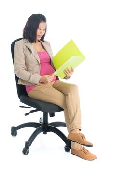 Full body six months pregnant Asian businesswoman reading file document sitting on chair, isolated on white background.