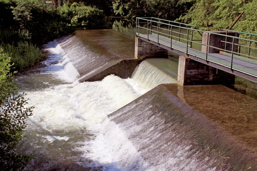 a dam retaining water from a swollen river with its bridge and waterfall