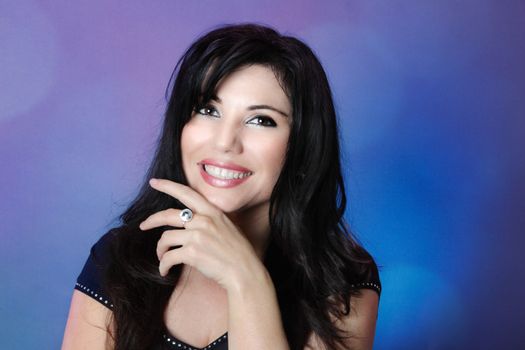 Smiling healthy and confident beautiful woman with glossy long black hair on a background of blues and pinks overlapping.