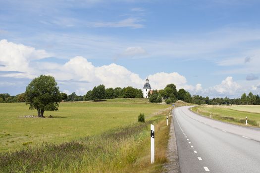 A road in Sweden leading past fields and a church