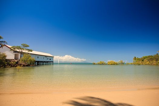 Beautiful tropical beach and bay with a calm ocean and golden sand and a building on a pier jutting into the water