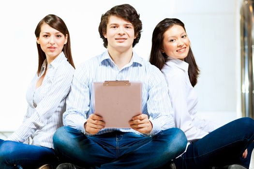 Image of three students in casual wear sitting on floor and smiling