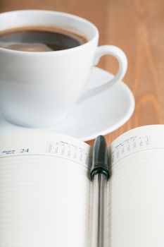 Notebook with pen and cup of coffee on a table. Top view