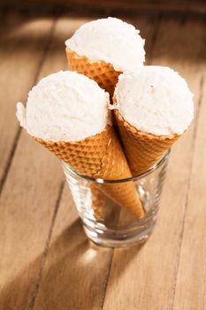 three vanilla ice cream scoops in waffle cones standing in a glass on wooden background