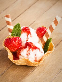 vanilla ice cream with strawberries and strawberry sauce in a waffle cup from top on wooden background