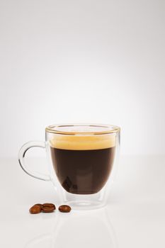 espresso in a glass cup with coffee beans on gray background