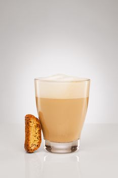 small cappuccino in a glass cup with a cantuccini cookie on gray background