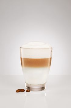 small latte macchiato in a glass cup with coffee beans on gray background