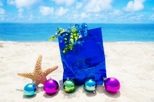 Starfish with Christmas balls and blue gift bag on sandy beach in sunny day- holiday concept