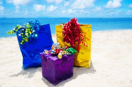Two Gift bags and gift box on sandy beach in sunny day- holiday concept