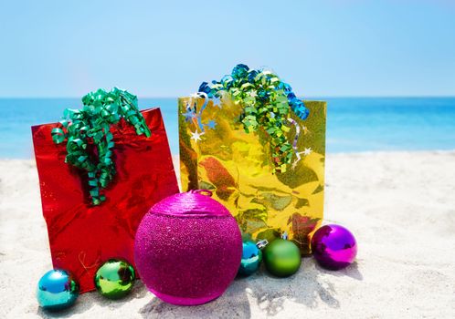 Gold and red gift bags with Christmas balsl on sandy beach in sunny day- holiday concept