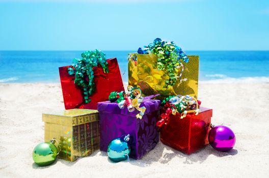 Three gift boxes and two gift bags with christmass balls on sandy beach in sunny day- holiday concept