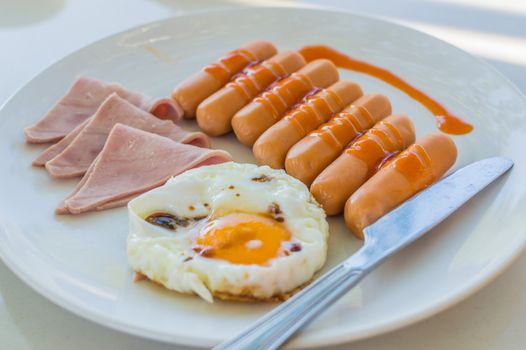 Wonderful breakfast.Sausage, ham and fried egg placed on a white dish.
