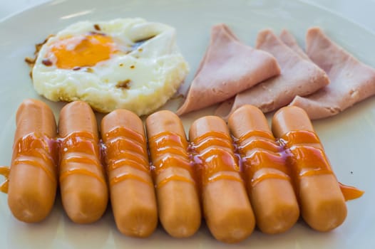 Wonderful breakfast.Sausage, ham and fried egg placed on a white dish.