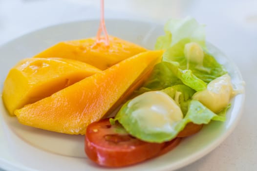 Fruit. 3 sliced ������mango pieces and various salads on a white dish.