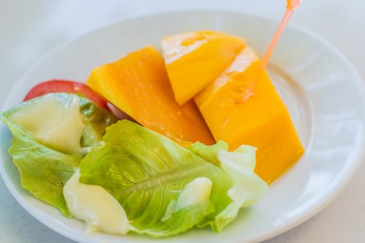 Fruit. 3 sliced ������mango pieces and various salads on a white dish.