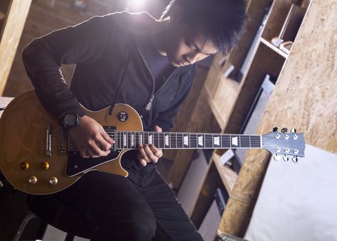 A young asian teenager playing electric guitar with a spotlight shining from the back.