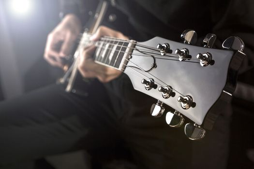 Close up of a man playing a guitar with spot light behind.