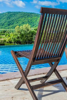 Wooden chair near the pool. With a mountain backdrop.