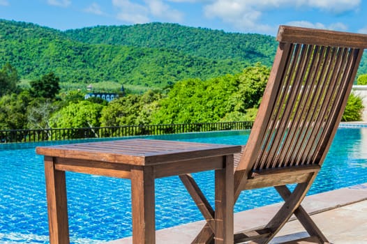 Wooden chair near the pool. With a mountain backdrop.