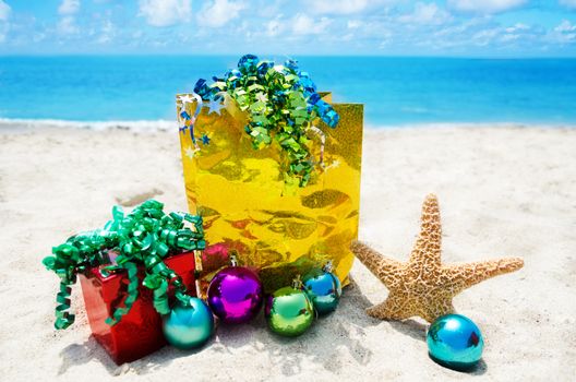 Starfish with gift box and bag and christmas balls on sandy beach in sunny day- holiday concept