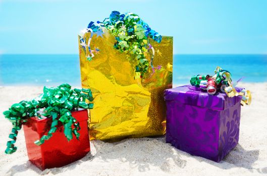 Gold gift bag and two gift boxes on sandy beach in sunny day- holiday concept