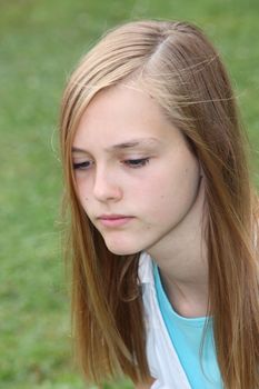 Thoughtful sad teenage girl with a serious expression and downcast eyes, closeup head portrait outdoors against grass