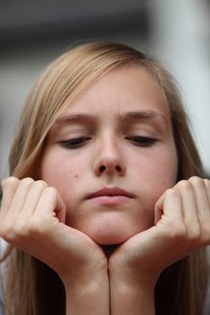 Cross young teenager with her chin resting on her hands, a serious expression and downcast eyes, close up headshot
