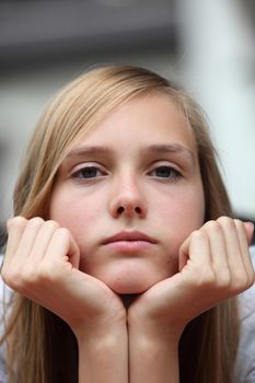 Bored young teenage girl staring at the camera with her chin resting on the palms of her hands