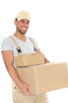 Confident young man in dungarees and a cap carrying plain brown cardboard boxes and smiling at the camera