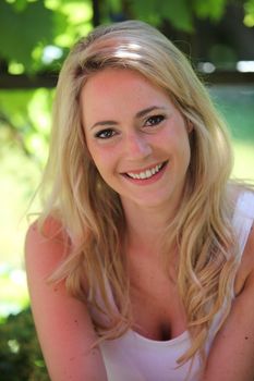 Happy friendly blond woman sitting outdoors in the shade of a tree on a hot summer day smiling at the camera